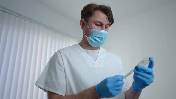 Concentrated Serious Doctor Filling Syringe with Coronavirus Vaccine Standing in Vaccination Center