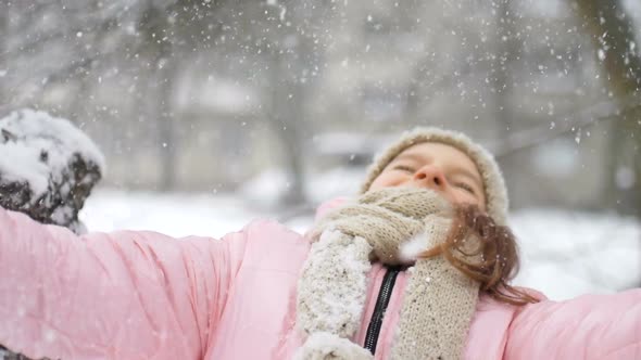 Winter Portrait of a Kid Girl in Pink Coat Wearing Beige Hat and Mittens Playing Outdoor in Snowy