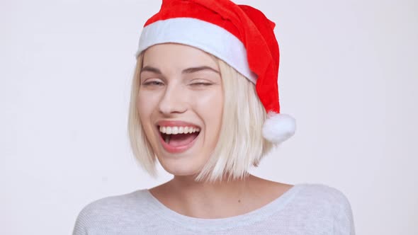 Young Beautiful Blonde Girl in Christmas Hat Smiling Winking Sending Kisses Ovwer White Background