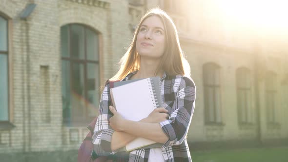 Smiling Woman Standing with Textbooks Near the University Building