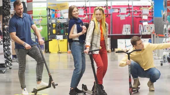 Group of Happy Caucasian Friends on Skooters in Sportswear Store