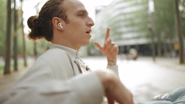 Pretty curly-haired man talking by phone in headphones