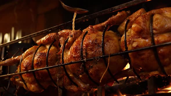 Roasted Chickens on Spit Grilled Over Wood Fire on Big Bbq Barbecue with a Spoon Spilling Sauce on