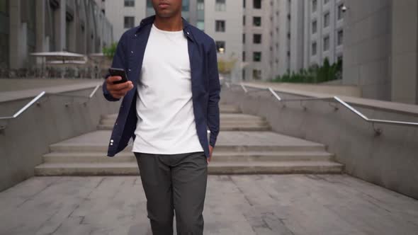 Ethnic Man with Laptop and Smartphone Walking on Street