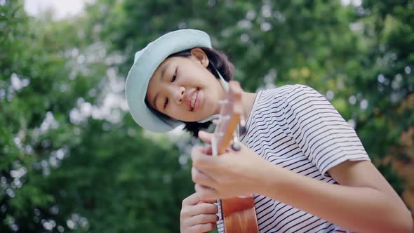 Beautiful Asian teenage girl playing at ukulele in the park, Slow motion