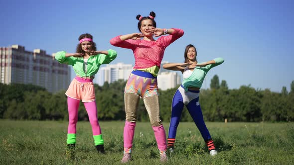 Wide Shot Slim Fit Retro Woman with Hair Buns Exercising with Friends Outdoors on Sunny Meadow