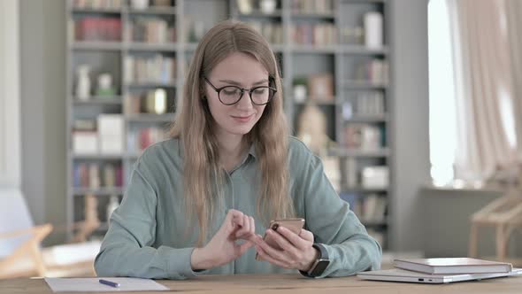 Young Female Student Using Smartphone While Sitting in Study Room