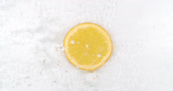 On a White Background, a Splash of Water Falls on a Slice of Lemon in Slow Motion