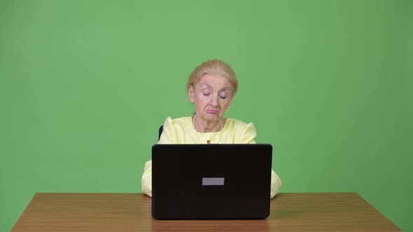 Beautiful Happy Senior Businesswoman Using Laptop and Thinking Against Wooden Table