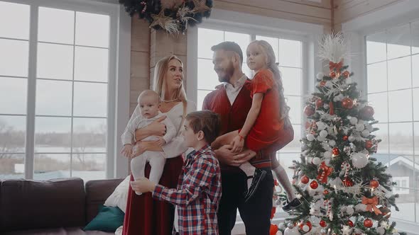 Family with Kids Dressed Up for Christmas Eve in Front of Tree Look at Camera