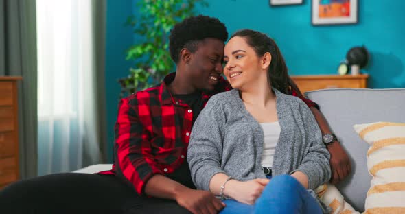 Happy Multiethnic Couple Bonding to Each Other and Smiling While Sitting on Couch