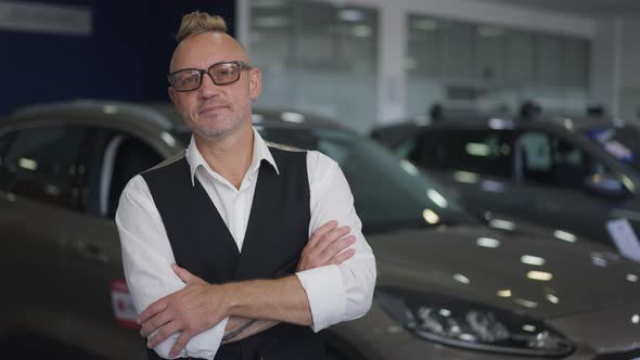 Portrait of Proud Wealthy Caucasian Man in Eyeglasses Standing in Car Dealership Looking at Camera