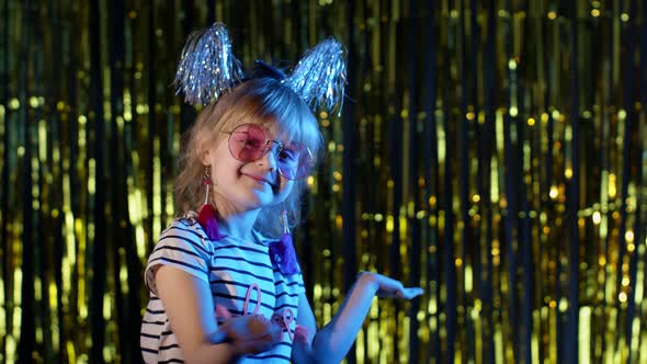 Stylish Teenager Kid Girl Standing on Backlit Blue Neon Lights and Points at Blank Space Agree Sign