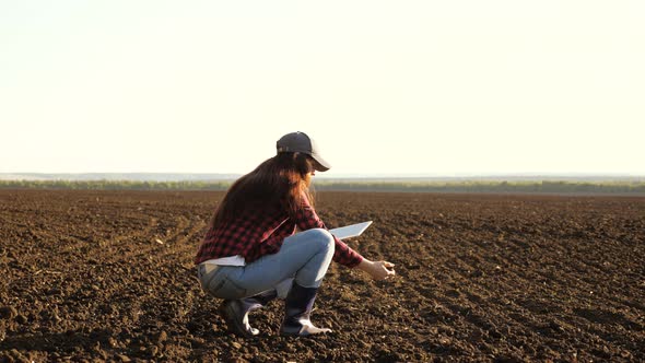 A Farmer Checks Quality of the Soil Before Sowing. Woman Farmer with a Tablet in Field Holds Earth