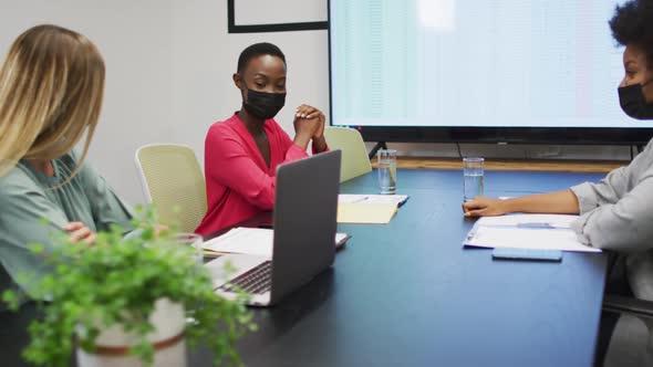 Three diverse businesswomen wearing face masks in discussion at an office meeting