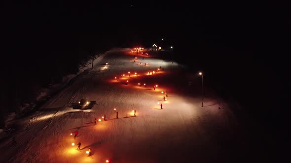 Zig Zag Skiers In The Night On Slope With Torchlights Parade