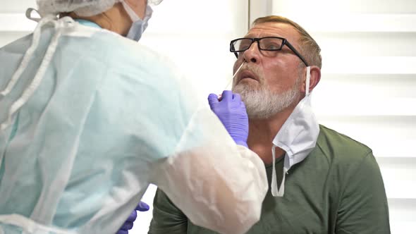 Lab Technician in a Protective Suit Takes a Swab From an Elderly Patient for Coronavirus.