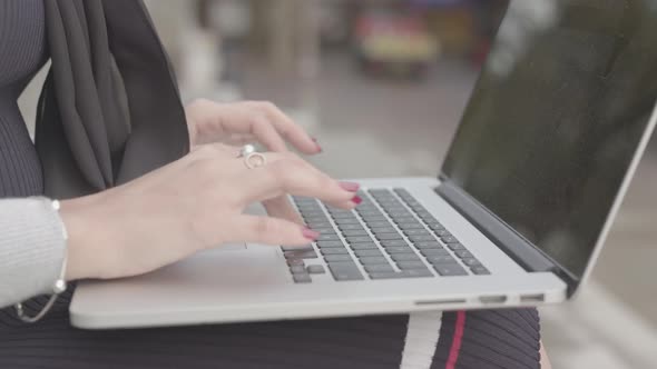 Close Up Shot Of Woman Sat Outside Typing/Working On Her Laptop As People Walk Past - Ungraded
