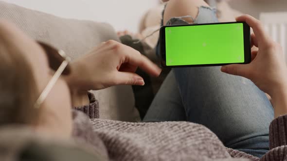 Young Woman Holding Smartphone Green Screen While Resting on the Sofa and Waving. Video Call