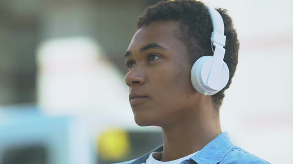 Upset Afro-American teen boy in headphones listening to music