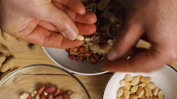 Slow motion footage of men's fingers peeling peanuts stacking them in a bowl. Close-up