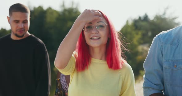 A Woman with Pink Hair Wearing Glasses Walks in the Middle of Her Friends Smiles Puzzles Them Tells