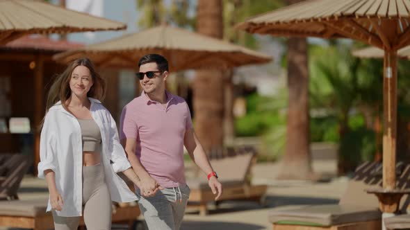 a Young Woman with Long Hair in a White Shirt and a Man in a Pink Tshirt Smile and Walk Along the