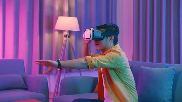 Young Asian Man Wearing Vr Headset At Living Room And Use Hand Touching , Cyan And Magenta Colors