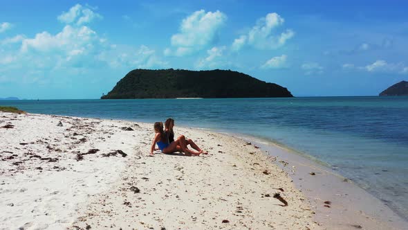 Beautiful young women relaxing on calm exotic beach with pristine white sand washed by calm blue sea