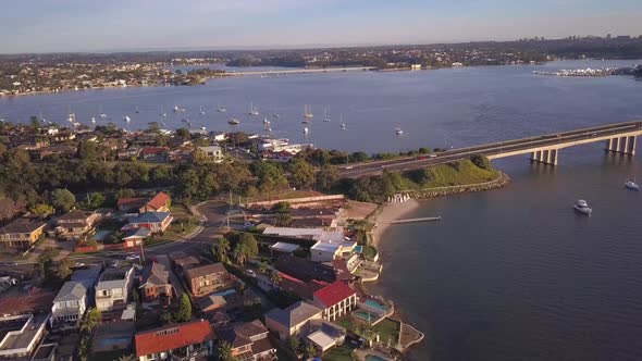 Aerial view of waterfront houses with ocean view and many boats and a long bridge. Drone panning rig