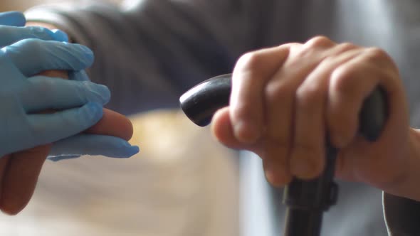 Close-up of the hand of a pensioner holding a stick cane, a doctor in gloves shakes hands with an el