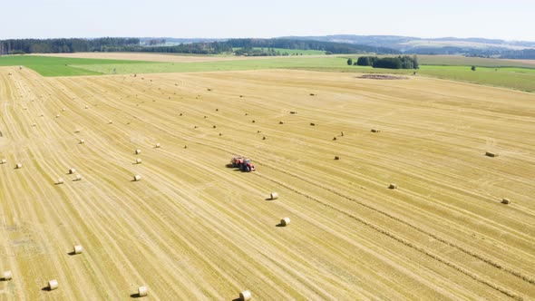 Aerial Drone Shot  a Tractor Drives Through a Field with Hay Bales in a Rural Area on a Sunny Day