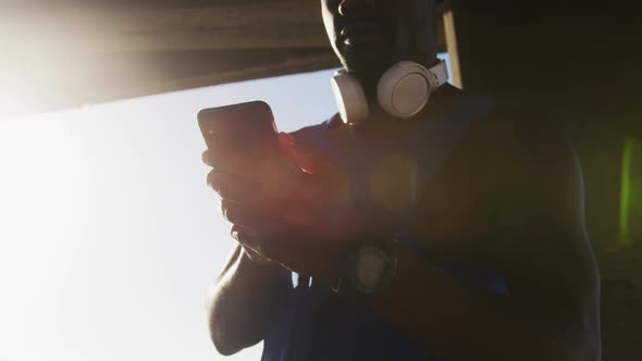 African american man checking smartphone taking break during exercise outdoors by the sea