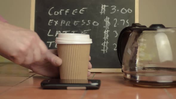 Hands holding a takeaway coffee to-go with cellphone close up