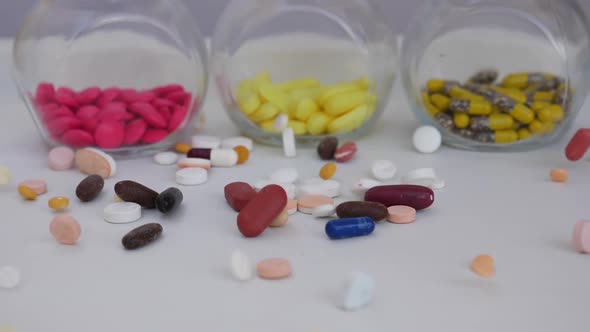 View of different tablets dropped over a white table with colorful tablets in glass bottle behind