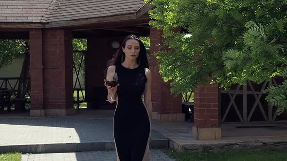 Elegant Woman with Glass of Wine Walking in Garden of Mansion