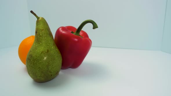 Fresh big green pear, red sweet bell pepper, juicy orange rotates slowly on a light blue background,