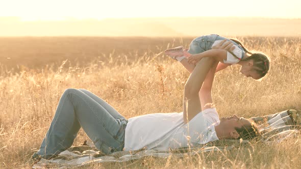 Dad Plays with His Little Daughter in the Park on a Blanket. Child Flies in the Arms of Dad, the Kid