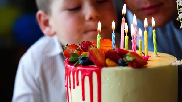 Child blowing candles on homemade baked cake, indoor. Colored party for school children