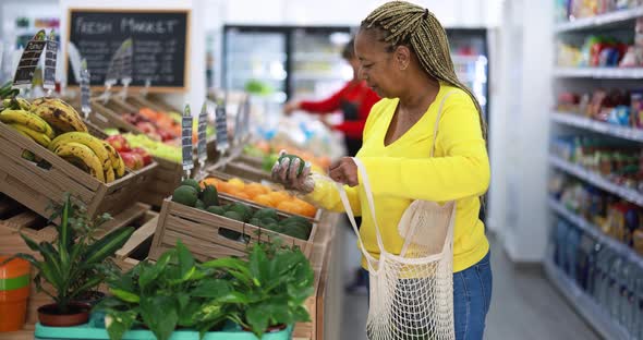 African female customer buying organic food fruits inside eco fresh market - Shopping concept