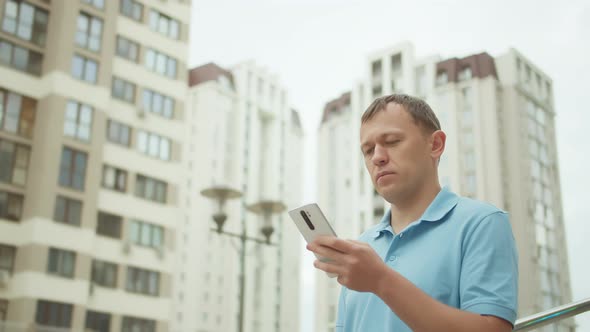 Attractive man typing text on a mobile phone, against the background of skyscrapers, tracking camera