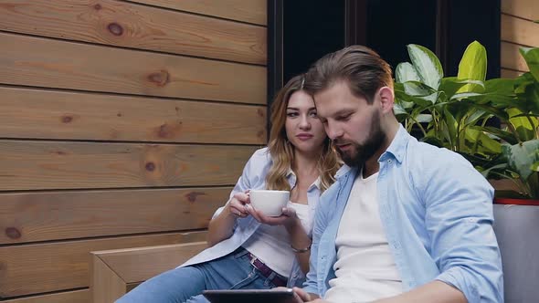 Happy Smiling Modern Couple Sitting in Cozy Lobby and Looking at Tablet PC