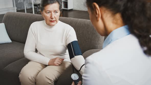 Back View of Unknown Female Doctor Measuring Blood Pressure of Aged Woman and Saying Her That It is