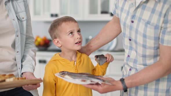 Portrait of Small Cute Male Child Picking Sea Roach From Meal Plate with Parents at Home Backdrop of