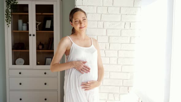 Pregnant Lady Touches Belly Near Brick Wall and Cabinet