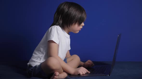 Boy Child in a White Tshirt and Shorts is Sitting on a Bed Against a Blue Wall of the House