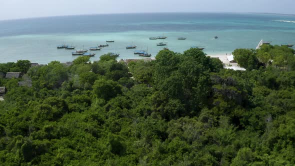 Anchored fishing boats on tropical beach with rainforest, drone shot.