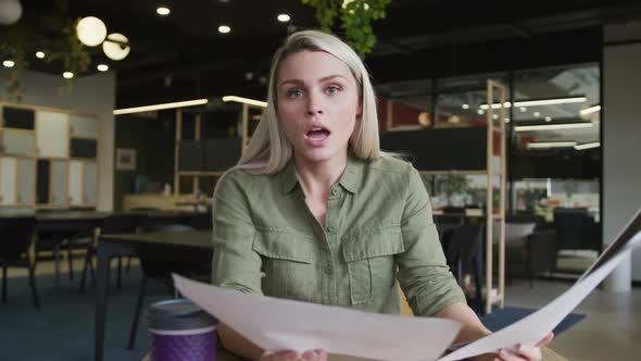 Caucasian businesswoman having a video chat going through paperwork in modern office