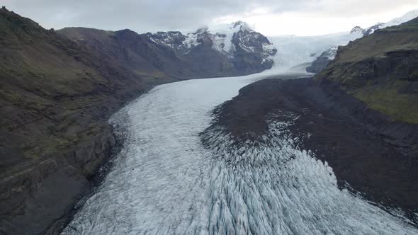 Aerial dolly out over glacier in Iceland flowing down narrow mountain valley.