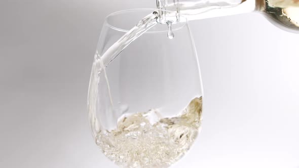 Pouring White Wine From a Clear Glass Into an Glass on a White Background